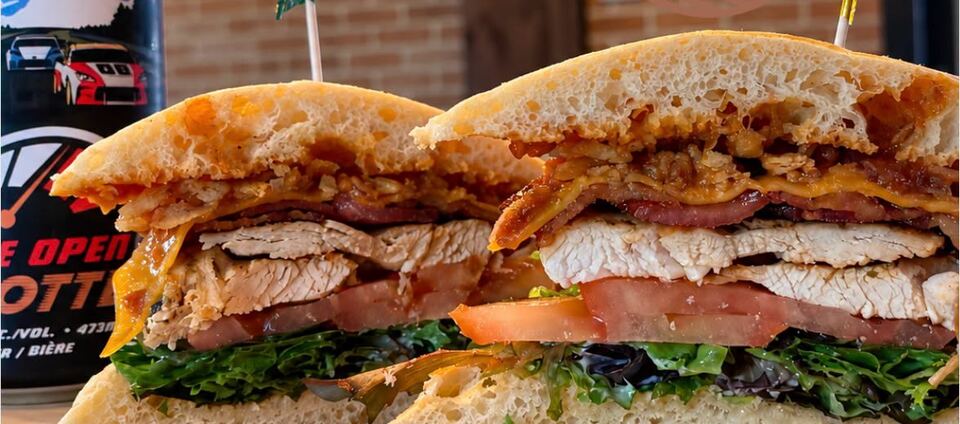 The Southern Club handheld: grilled chicken, bacon, cheddar and fried onions on ciabatta, with a tall can behind it