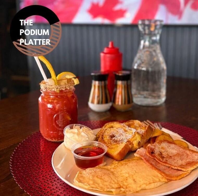 The Podium Platter breakfast plate: french toast, bacon, pancakes, with a Caesar drink on a red mat