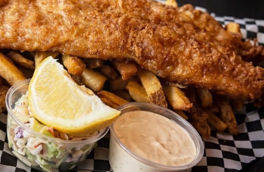 Beer-battered fish, fries, slaw and tartar with a lemon wedge on checkerboard paper