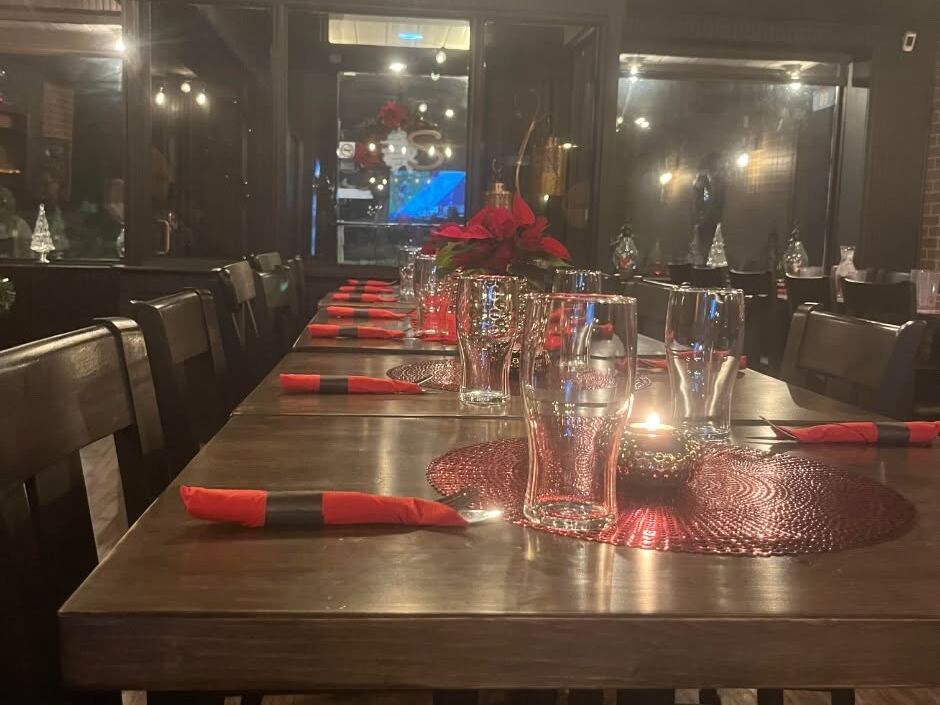 Dining room: a long dark table set with red napkins and glasses, dark wood and brick, string lights